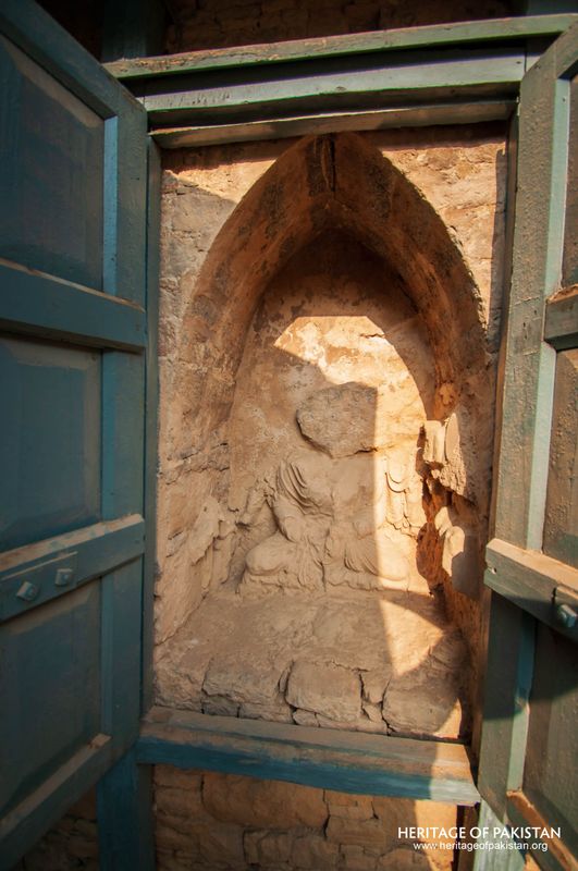 Sculpted figure protected within gated cell at heritage site.